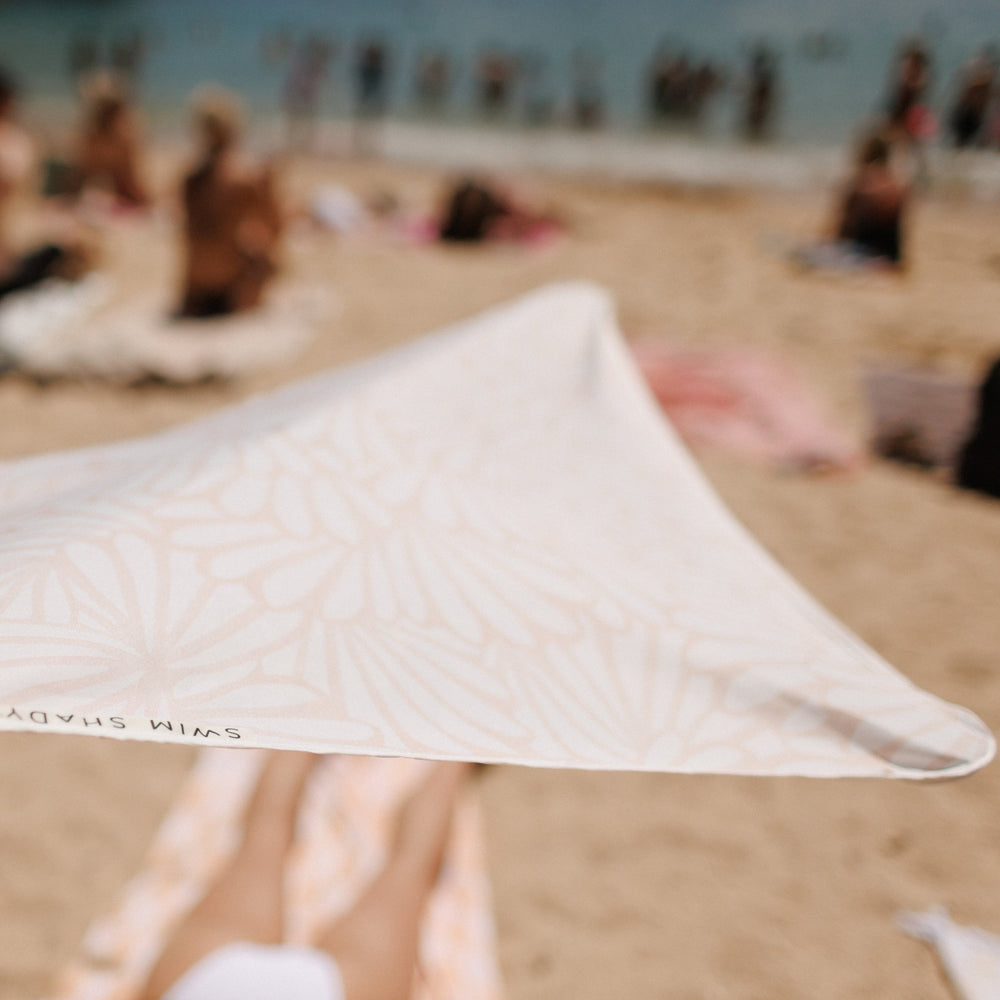 Woman relaxing on the sand under the cream Soothe Swim Shady beach canopy with a warm petal pattern